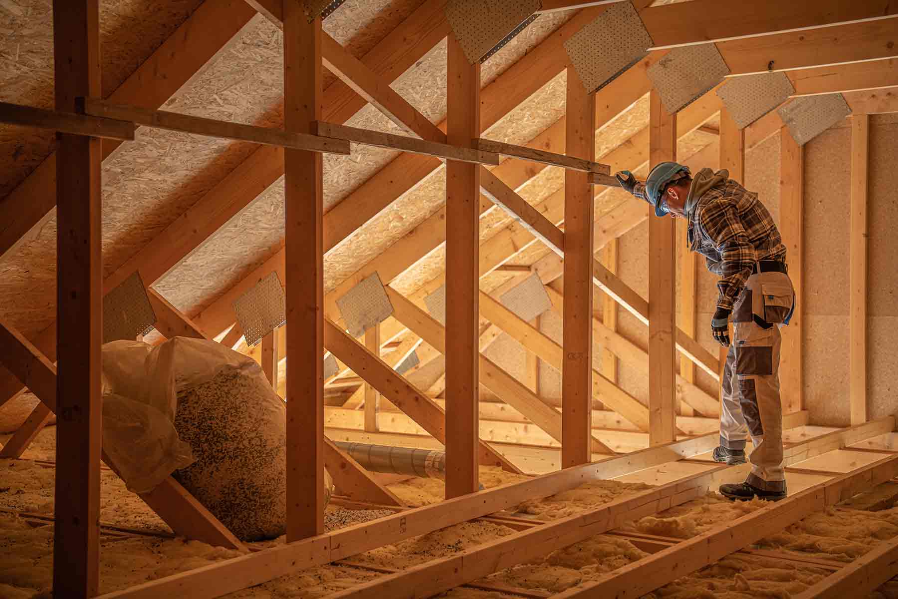 An inspector examines insulation in a residential attic, ensuring proper installation in the wooden framework