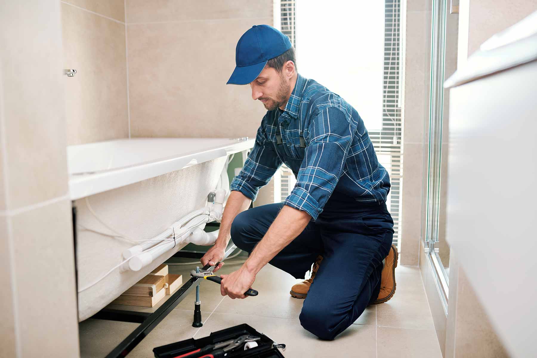 Professional plumber fixing bathtub plumbing in a modern residential bathroom Professional plumber fixing bathtub plumbing in a modern residential bathroom