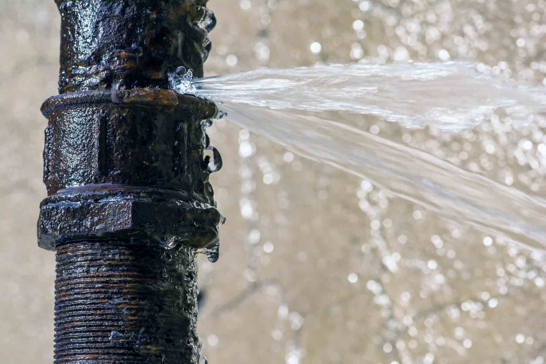 A rusted burst pipe leaking water in a home