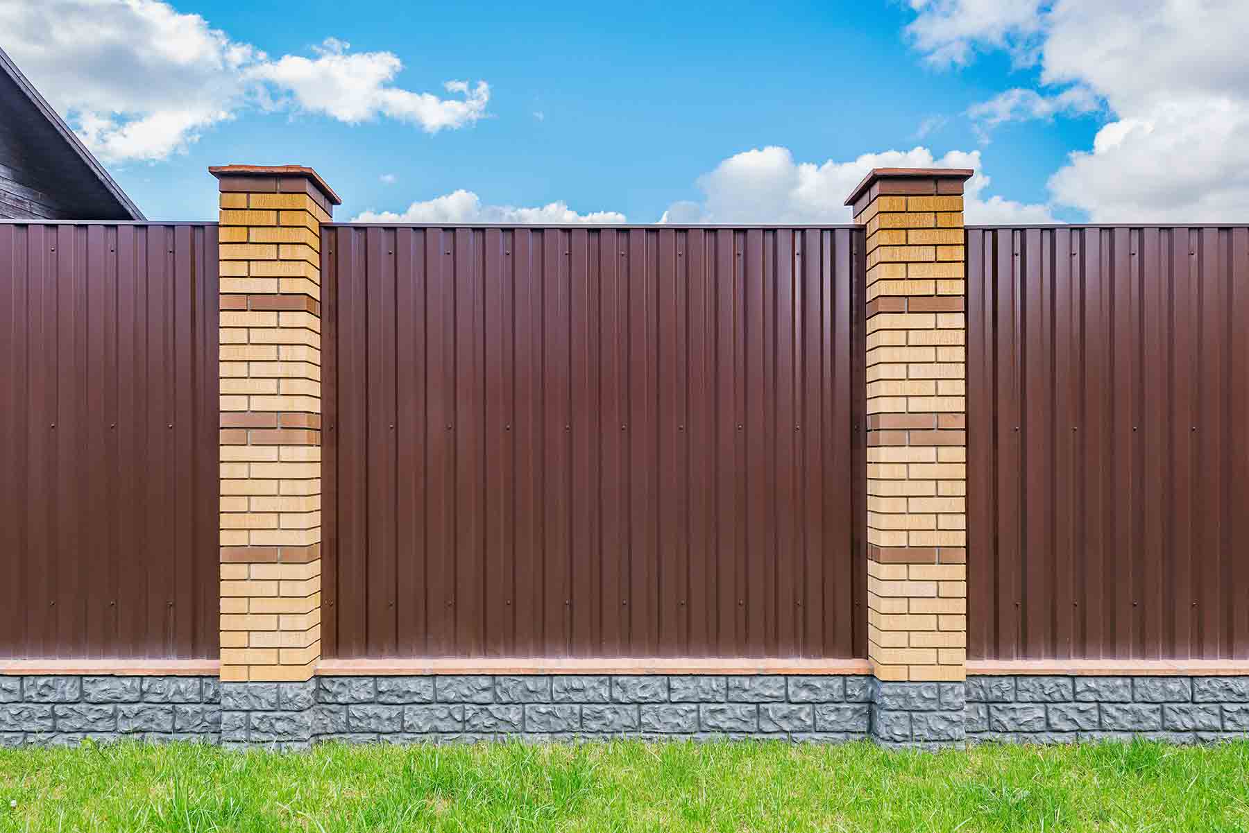 A brown corrugated metal fence installed with two vertical posts in a residential backyard