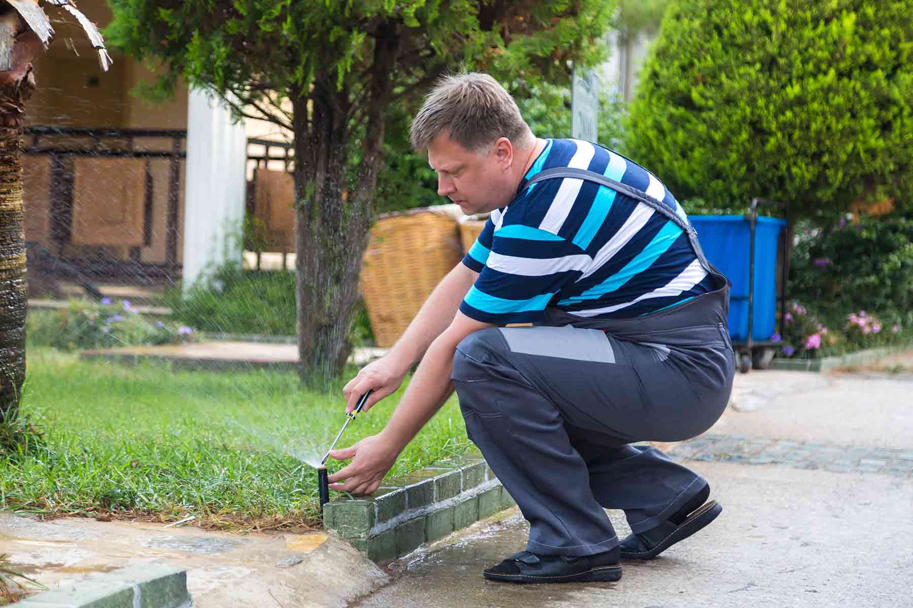 A technician adjusting a sprinkler head during lawn irrigation system repair A technician adjusting a sprinkler head during lawn irrigation system repair