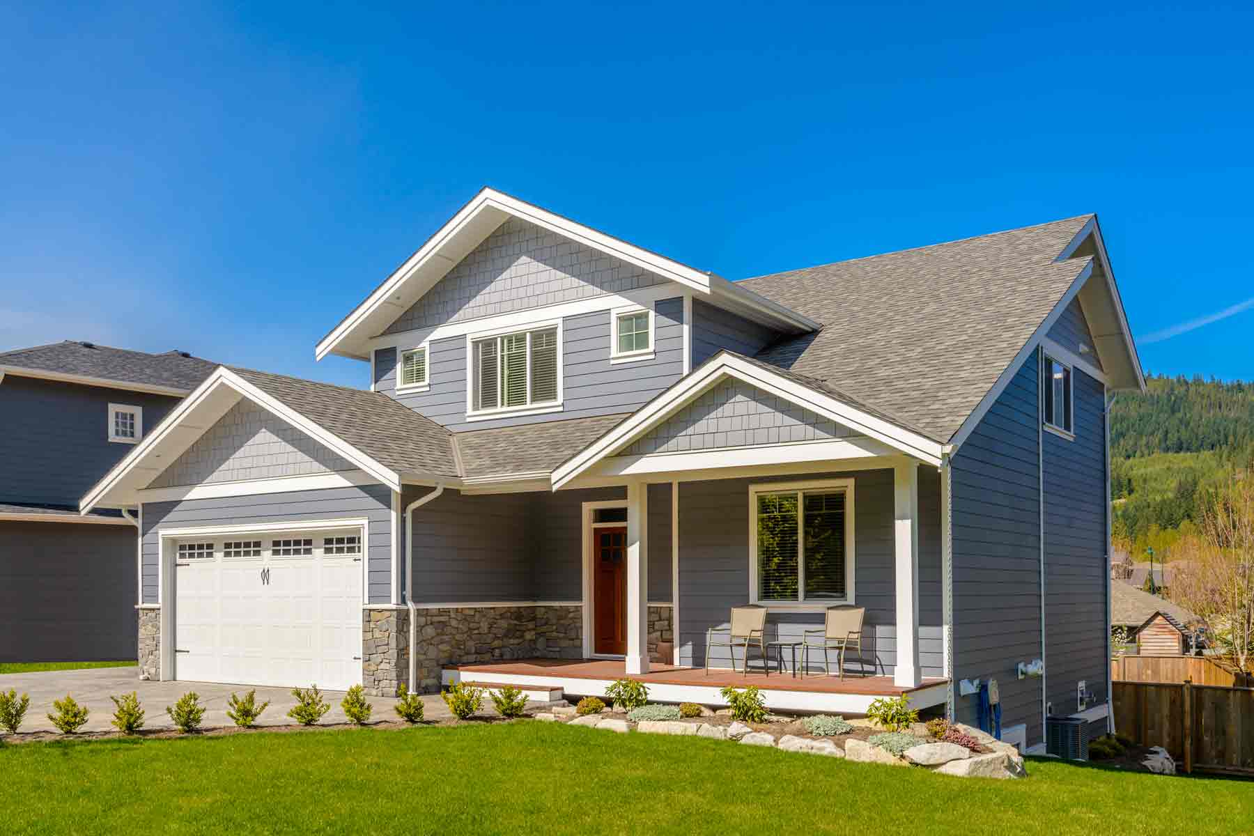 A new house with vinyl and composite shake siding, stone siding accents, a front porch, and a two-car garage. A new house with vinyl and composite shake siding, stone siding accents, a front porch, and a two-car garage.