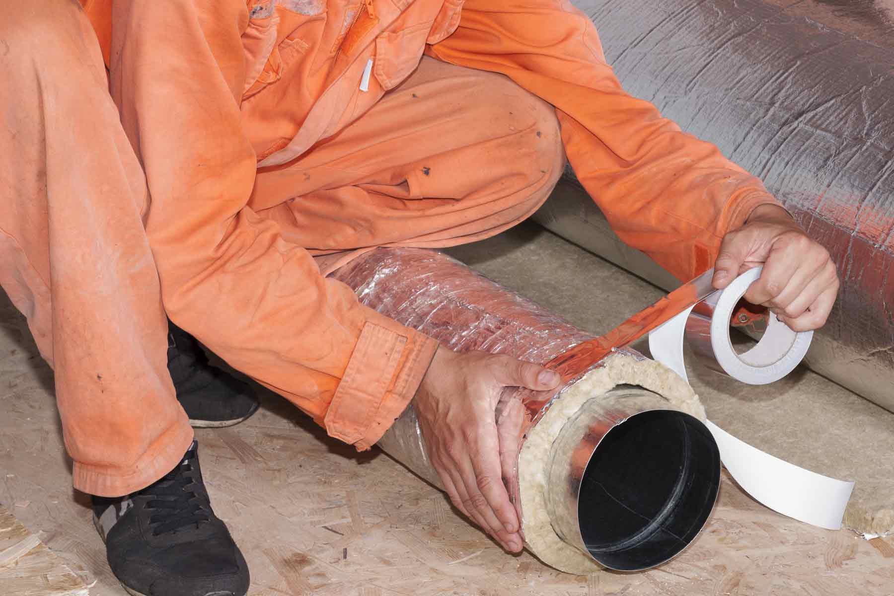 A worker wrapping an HVAC duct in fiberglass insulation