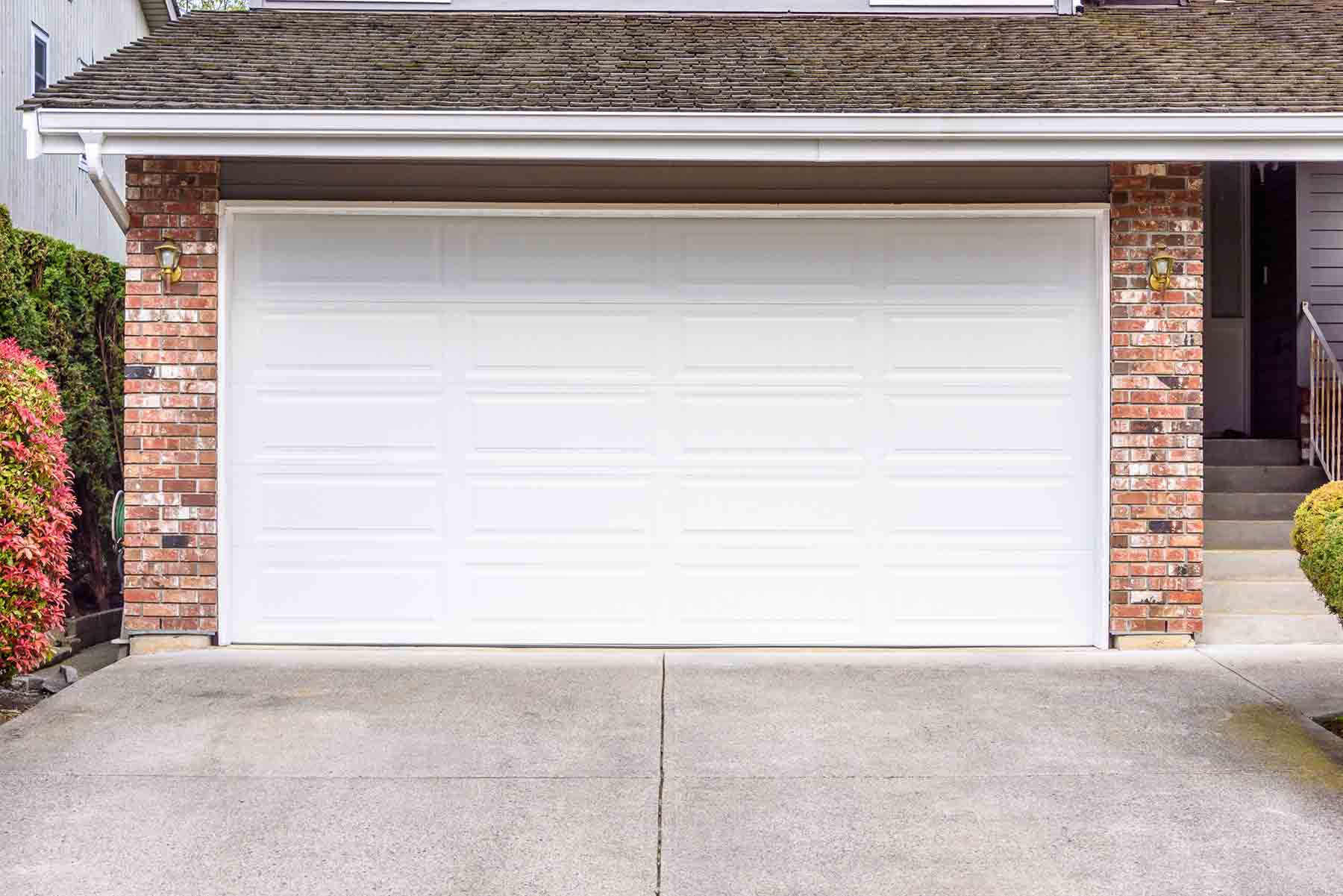 Front view of a closed white garage door on a brick-trimmed suburban home