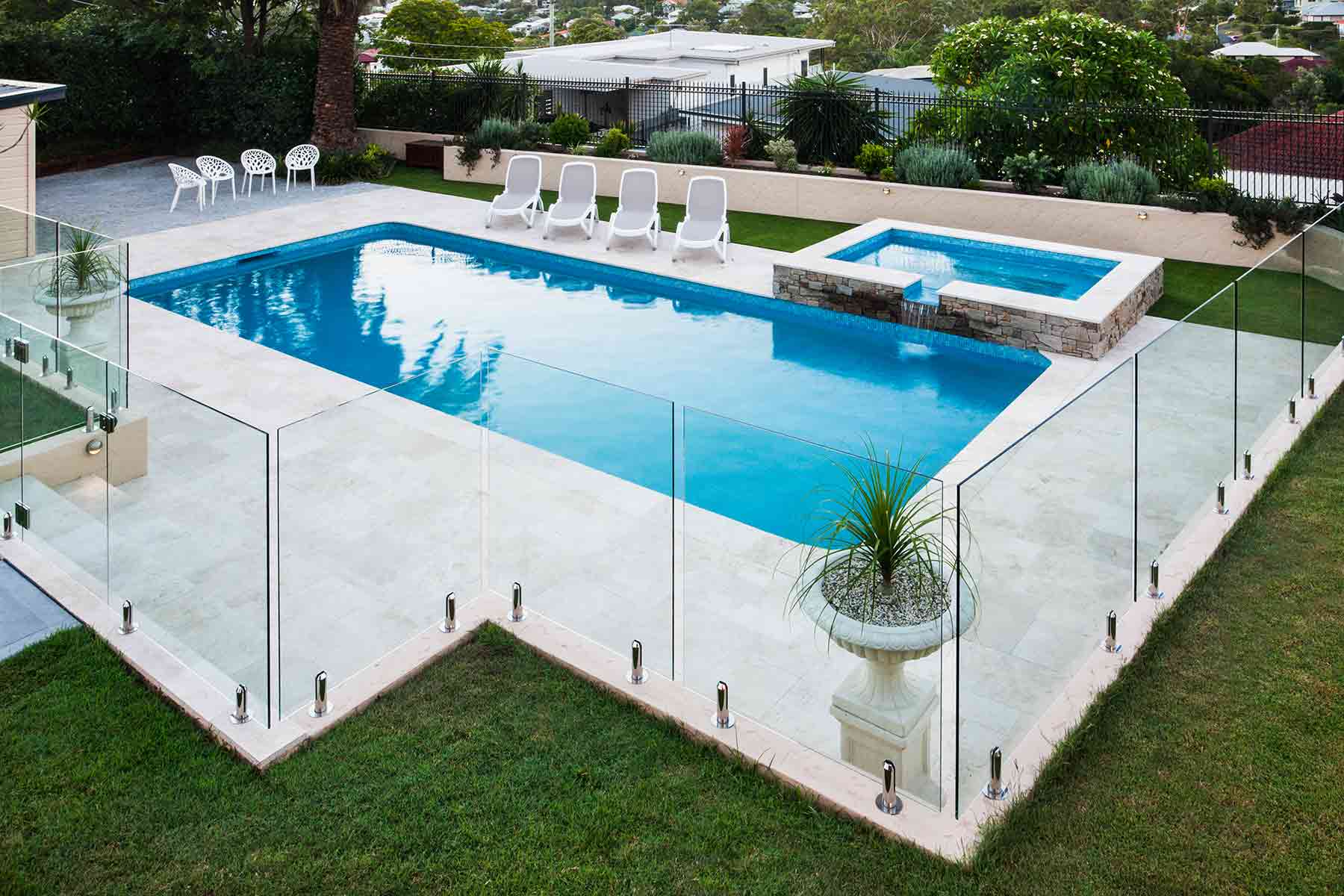 A modern swimming pool surrounded by a glass fence with lounge chairs nearby