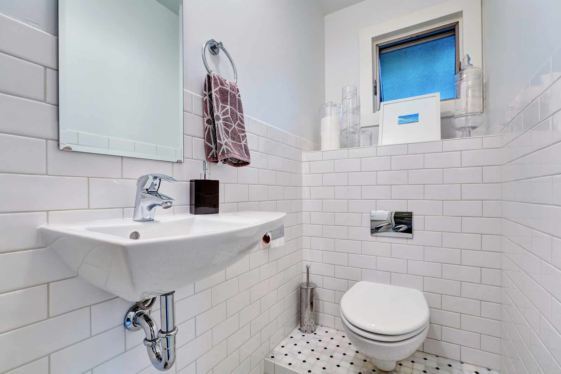 A white half bathroom interior with tile wall trim, washbasin, and a mirror