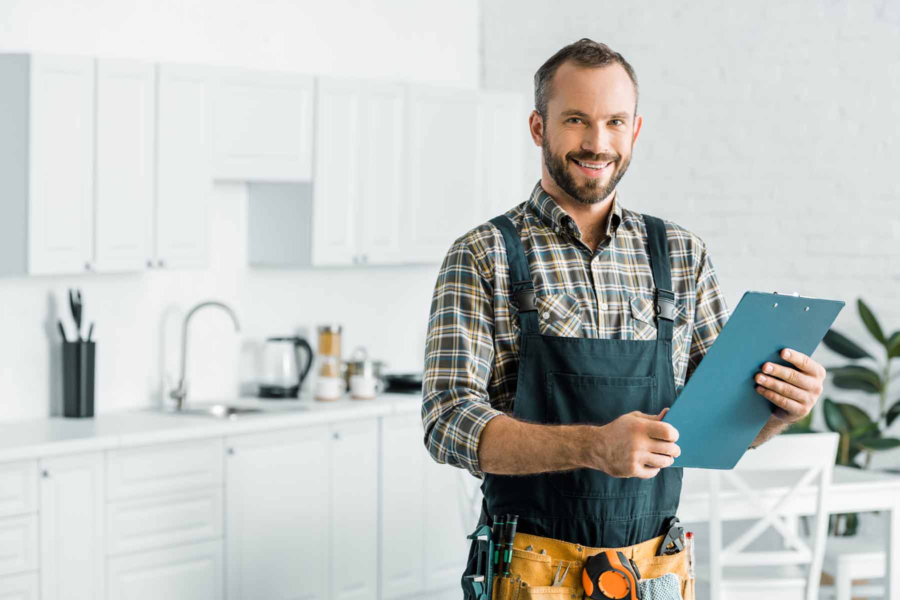 A smiling homeowner with a tool belt and clipboard with a home maintenance checklist A smiling homeowner with a tool belt and clipboard with a home maintenance checklist