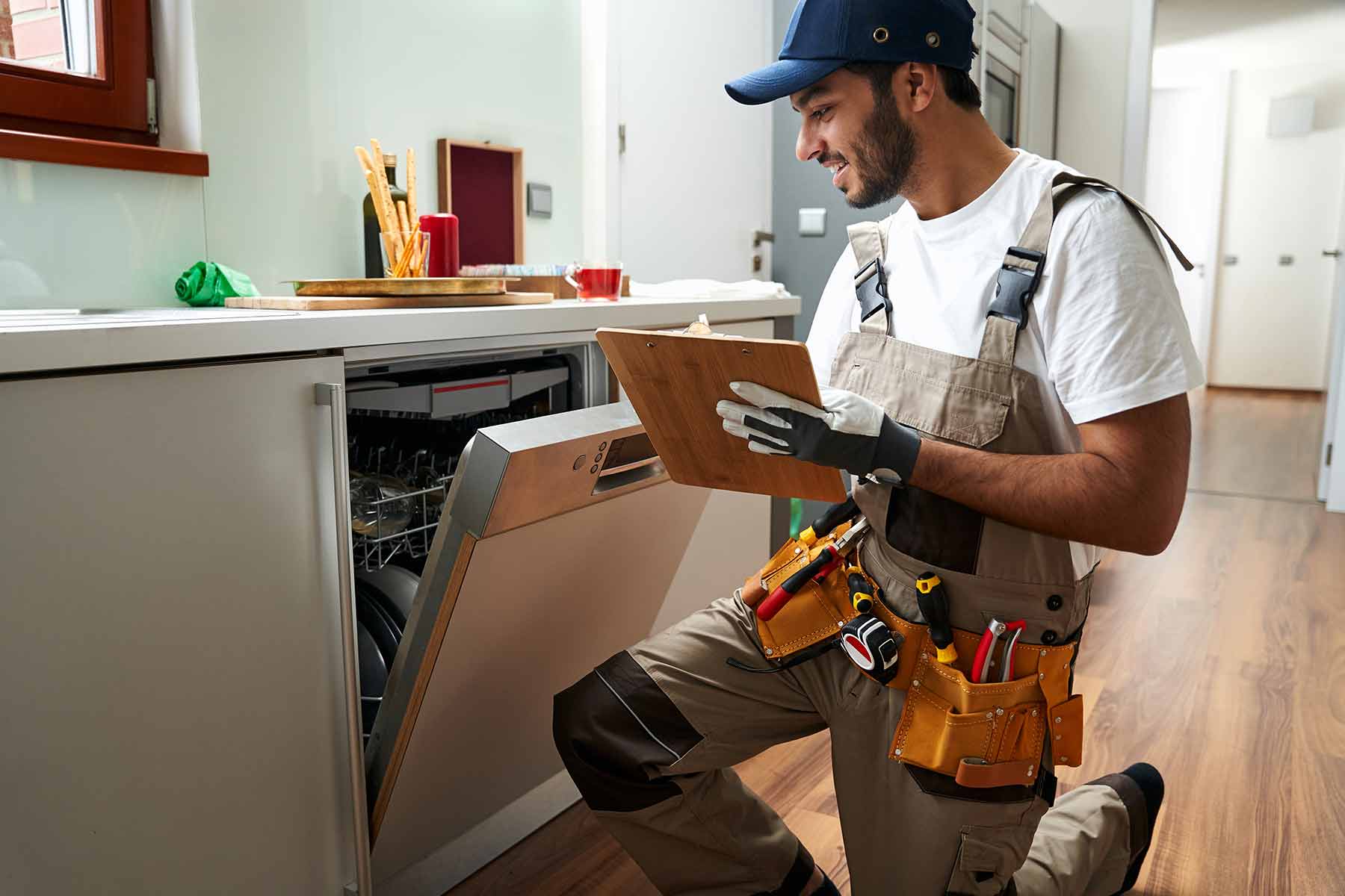A handyman performing a dishwasher inspection during a home maintenance service