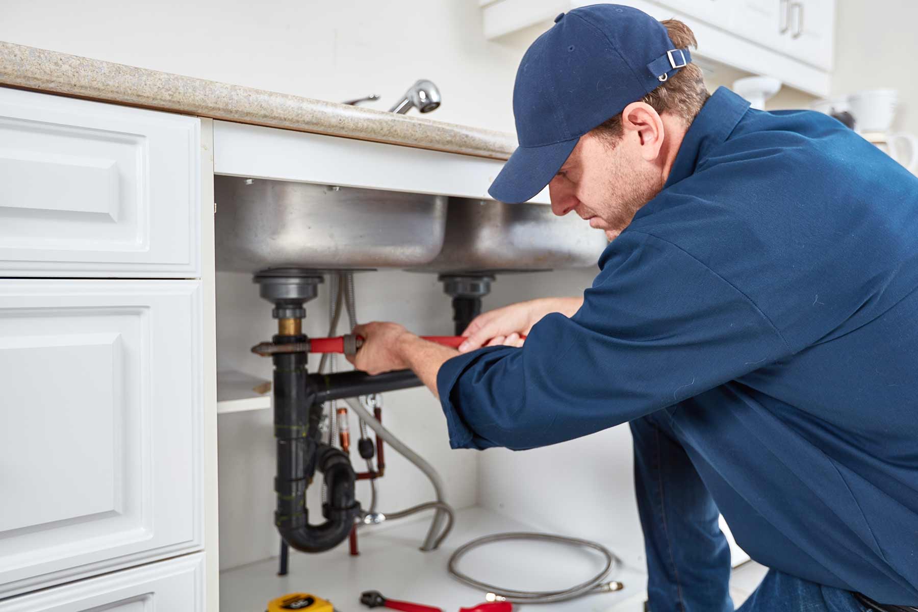 A professional plumber repairing a kitchen sink pipe using a wrench