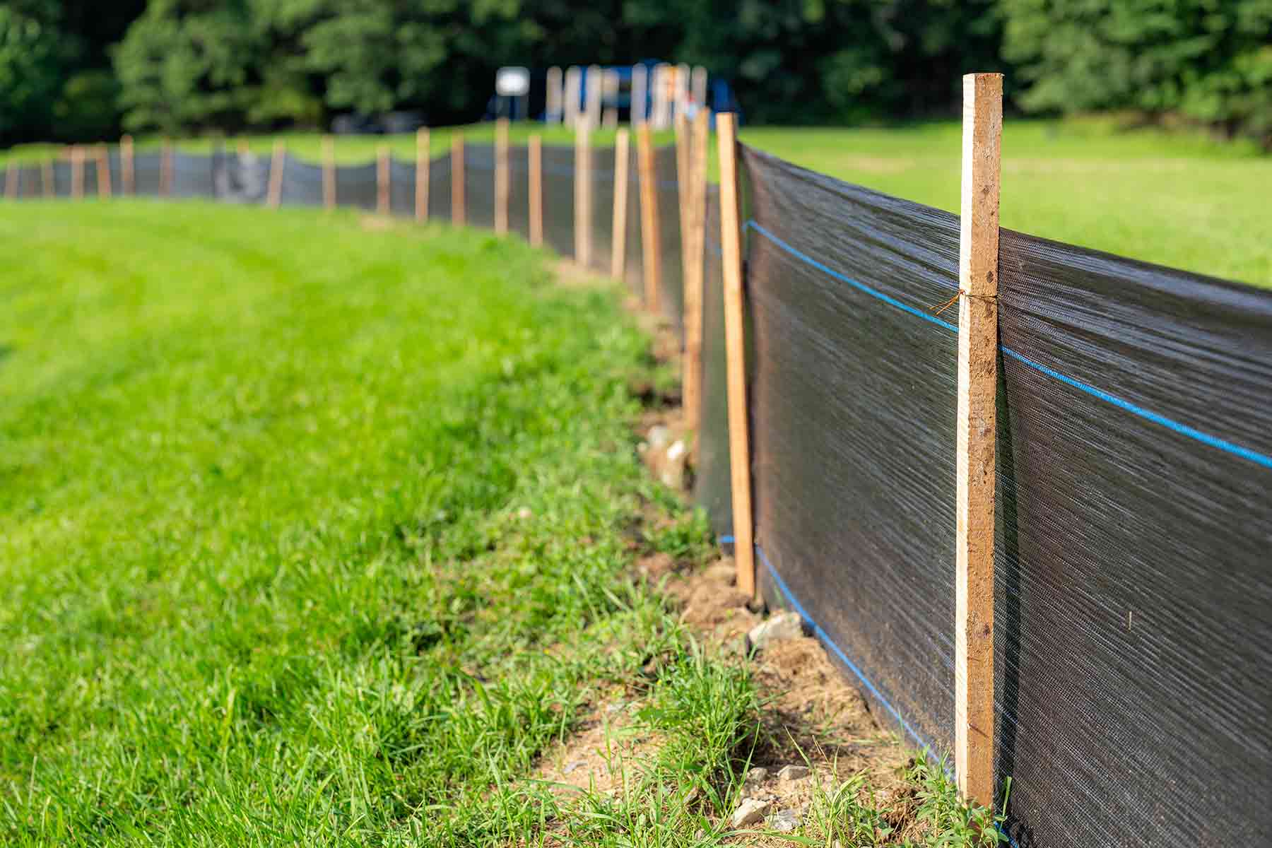Black silt fence fabric installed with wooden posts in a grassy field