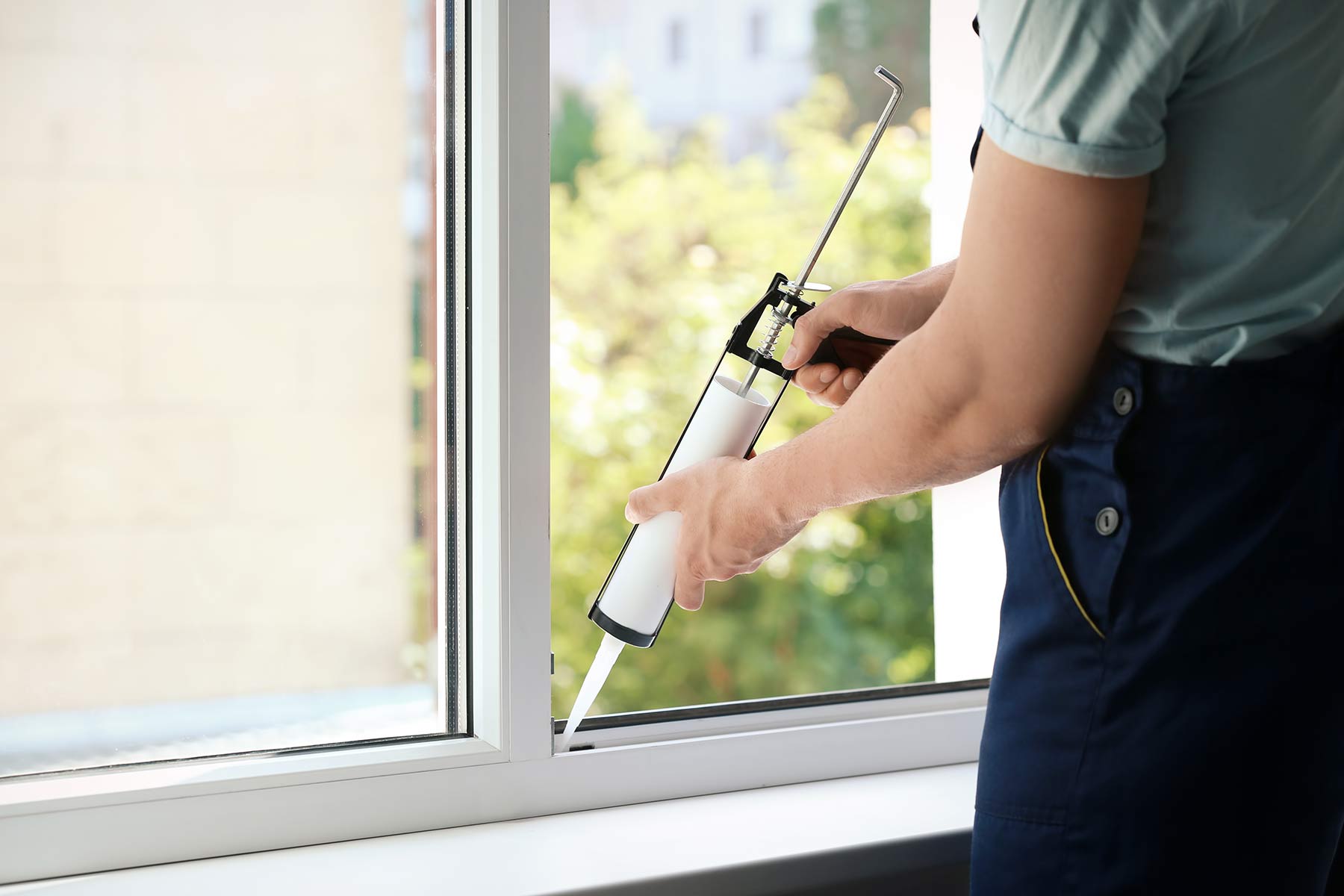 Close-up of a technician's hand using a caulking gun to repair a window seal